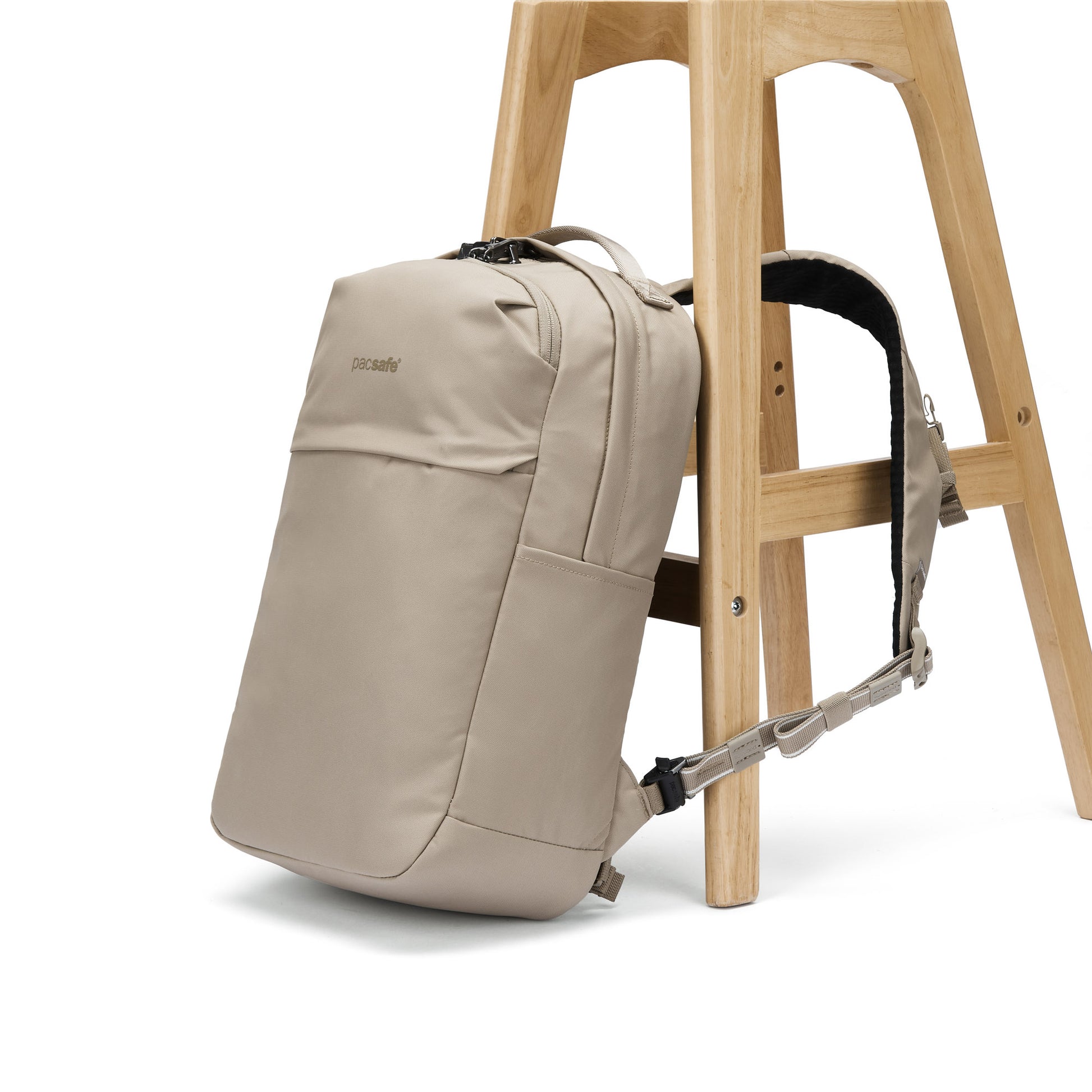The Pacsafe® V 20L Anti-theft City Backpack in beige hangs from a wooden stool by one strap.