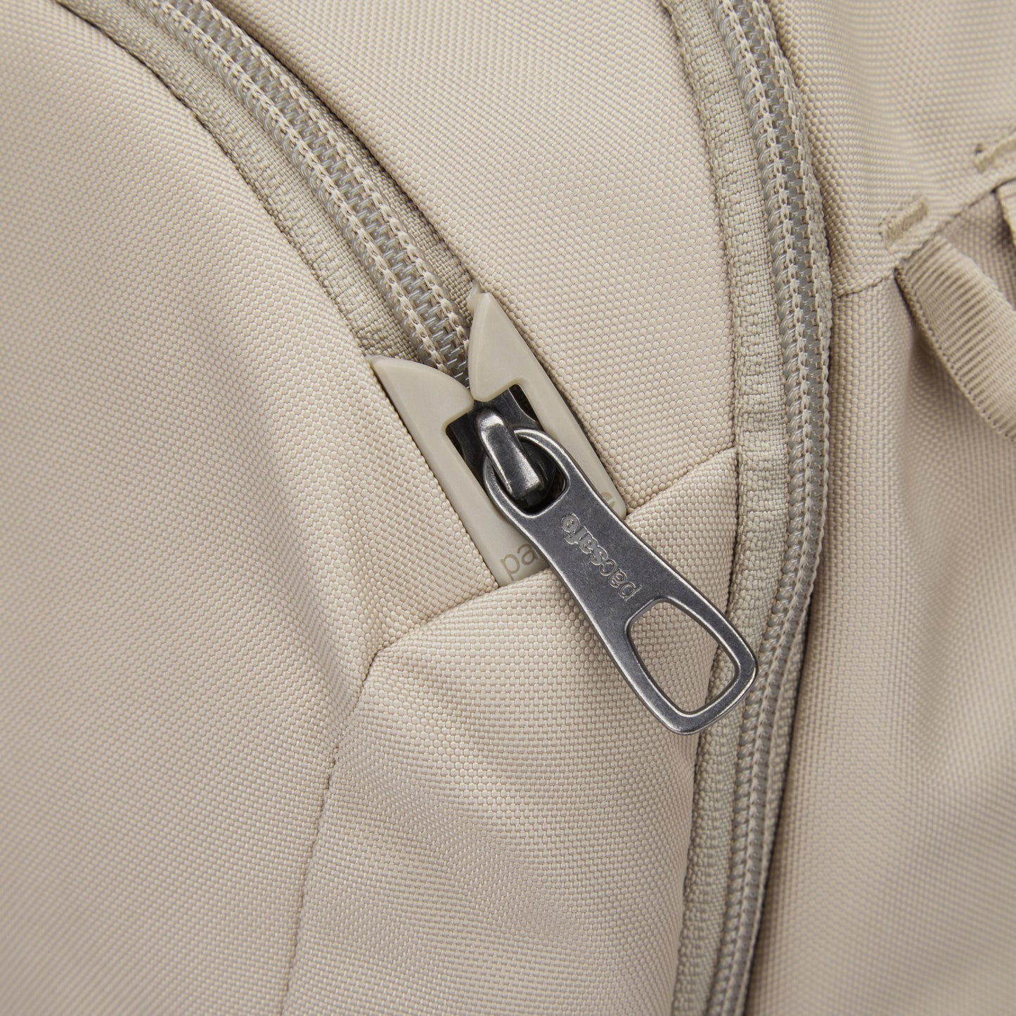 Close-up of Pacsafe® V 26L Anti-theft Tour Backpack in beige, made from recycled polyester with a metal zipper pull.