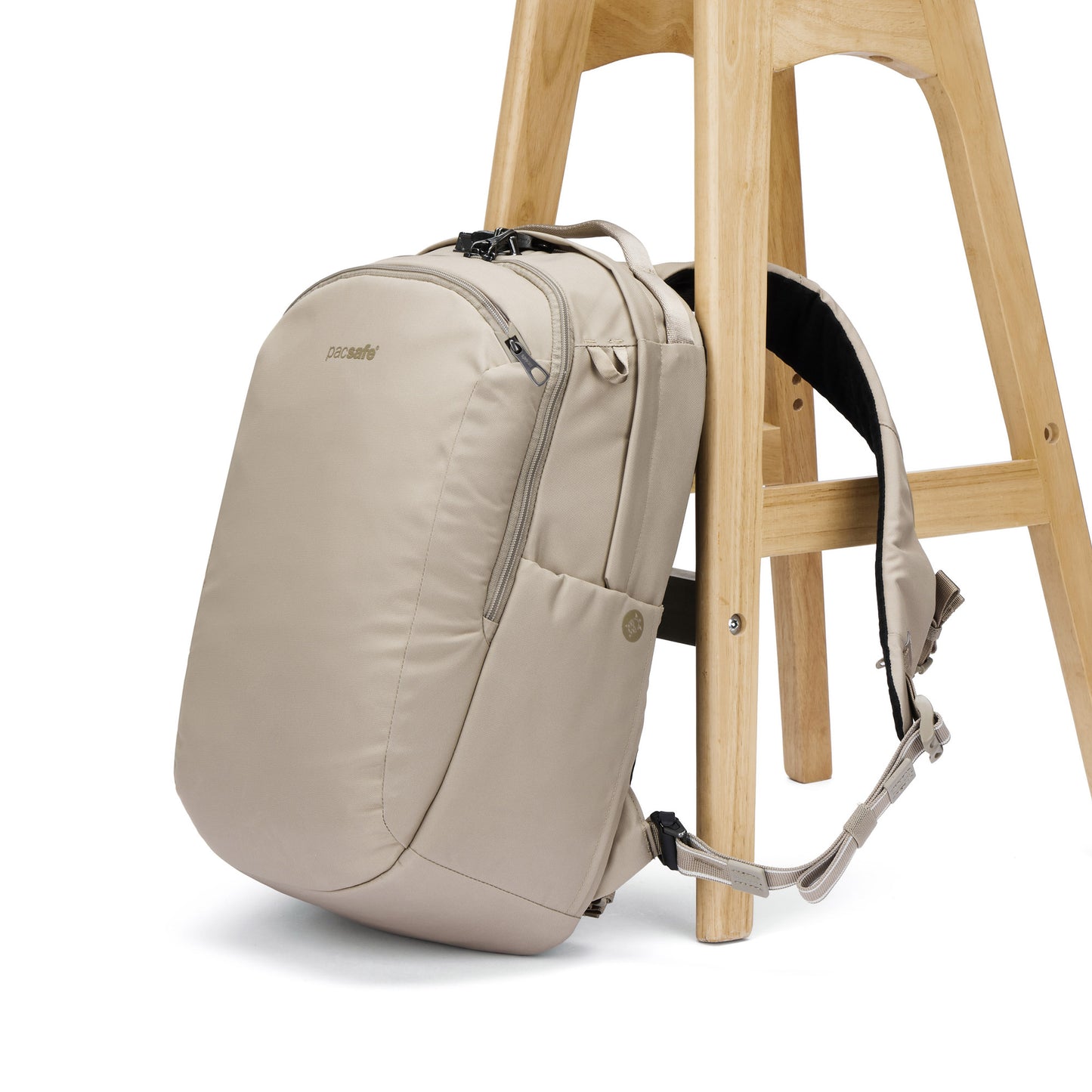 The Pacsafe® V 26L Anti-theft Tour Backpack in beige leans on a wooden stool against a white background.
