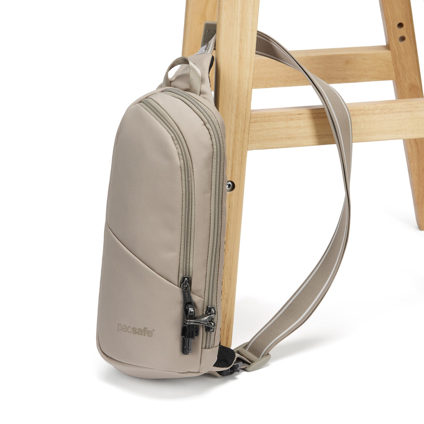 The Pacsafe® V sling pack, in beige, with strap around a chair leg.