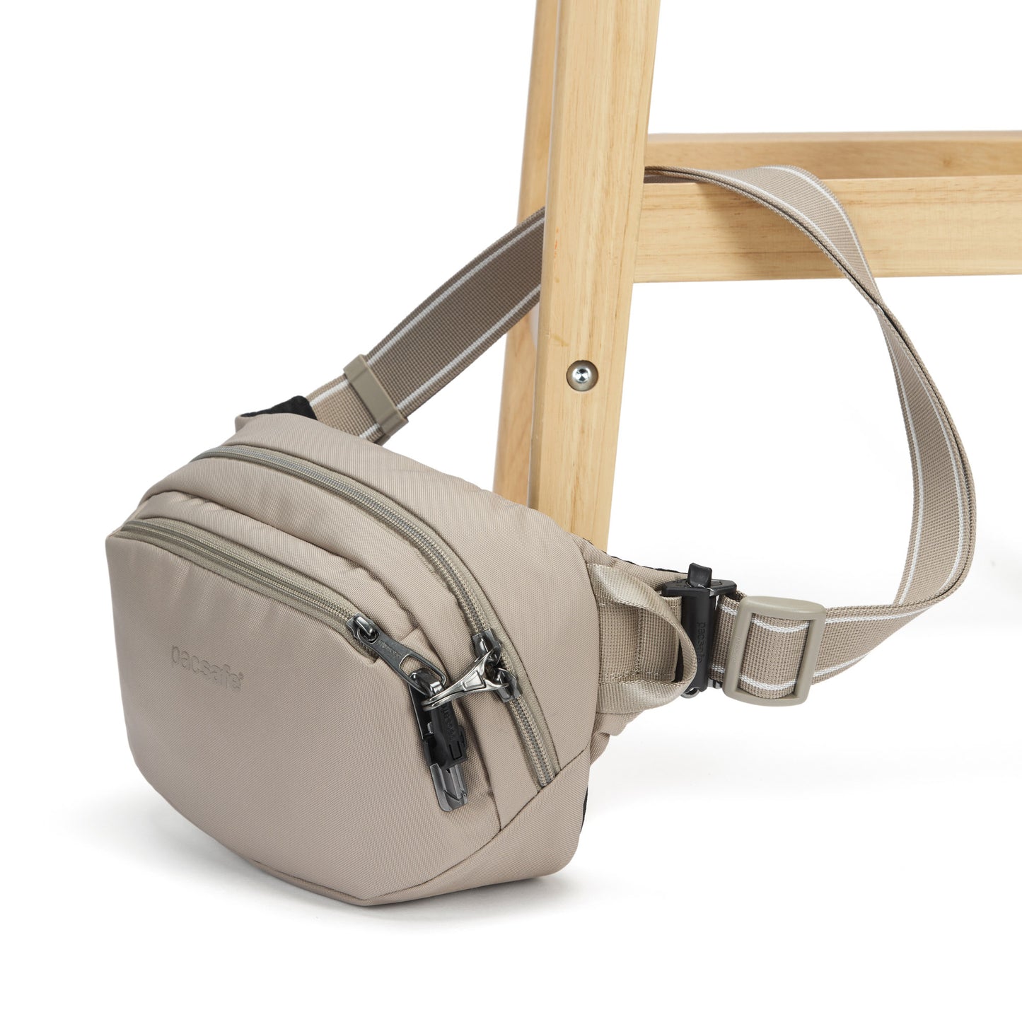 Pacsafe® V anti-theft hip pack in beige, with strap fastened to a chair leg.