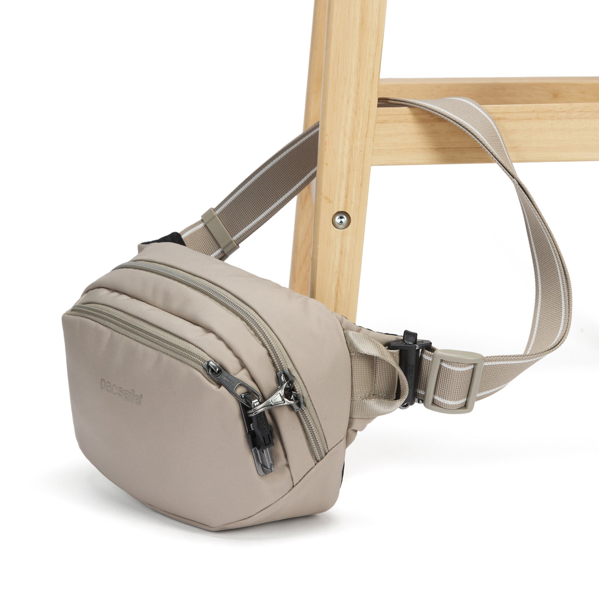 Pacsafe® V anti-theft hip pack in beige, with strap fastened to a chair leg.