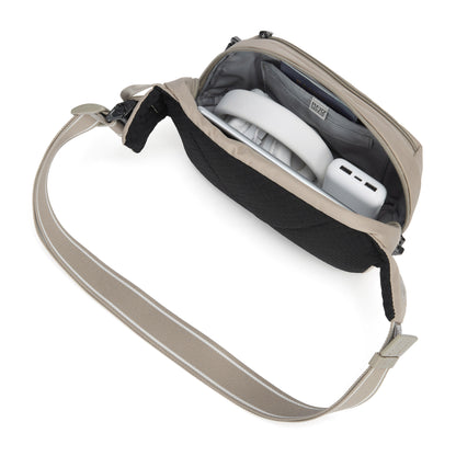 Pacsafe® V anti-theft hip pack in beige, top view with headphones and charger inside.