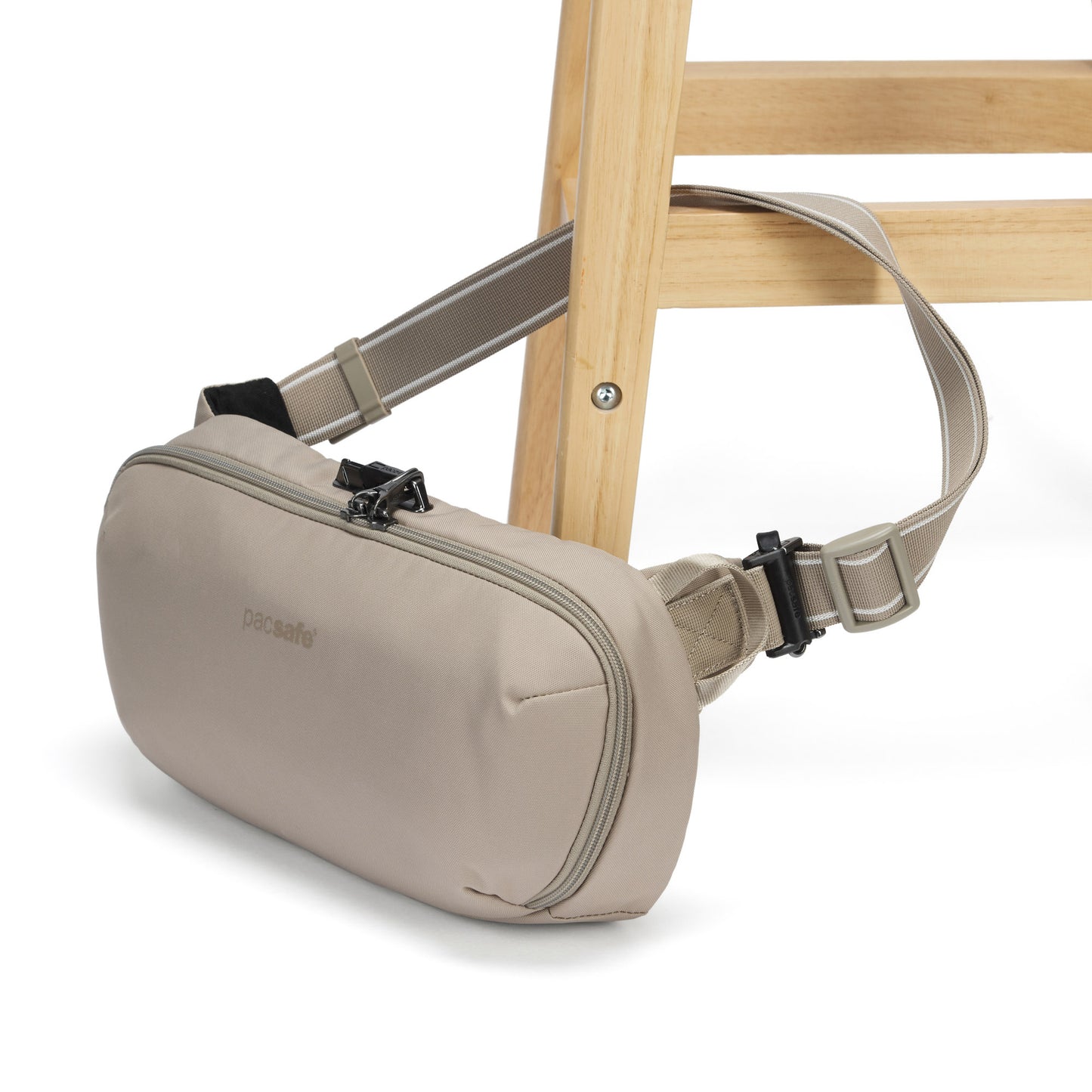 Pacsafe® V Anti-theft Urban Sling by Pacsafe, beige, with strap and buckle secured to a wooden chair leg.