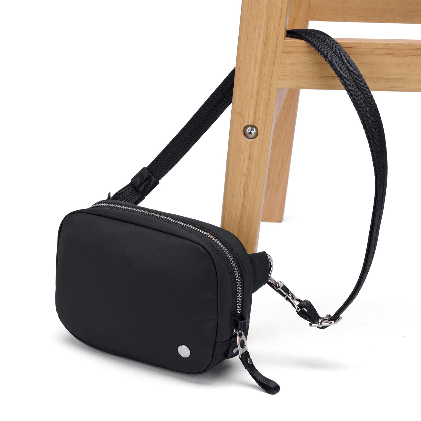The Pacsafe® W Anti-theft Micro Sling in black, with RFID blocking, hangs by its strap from a wooden chair leg.