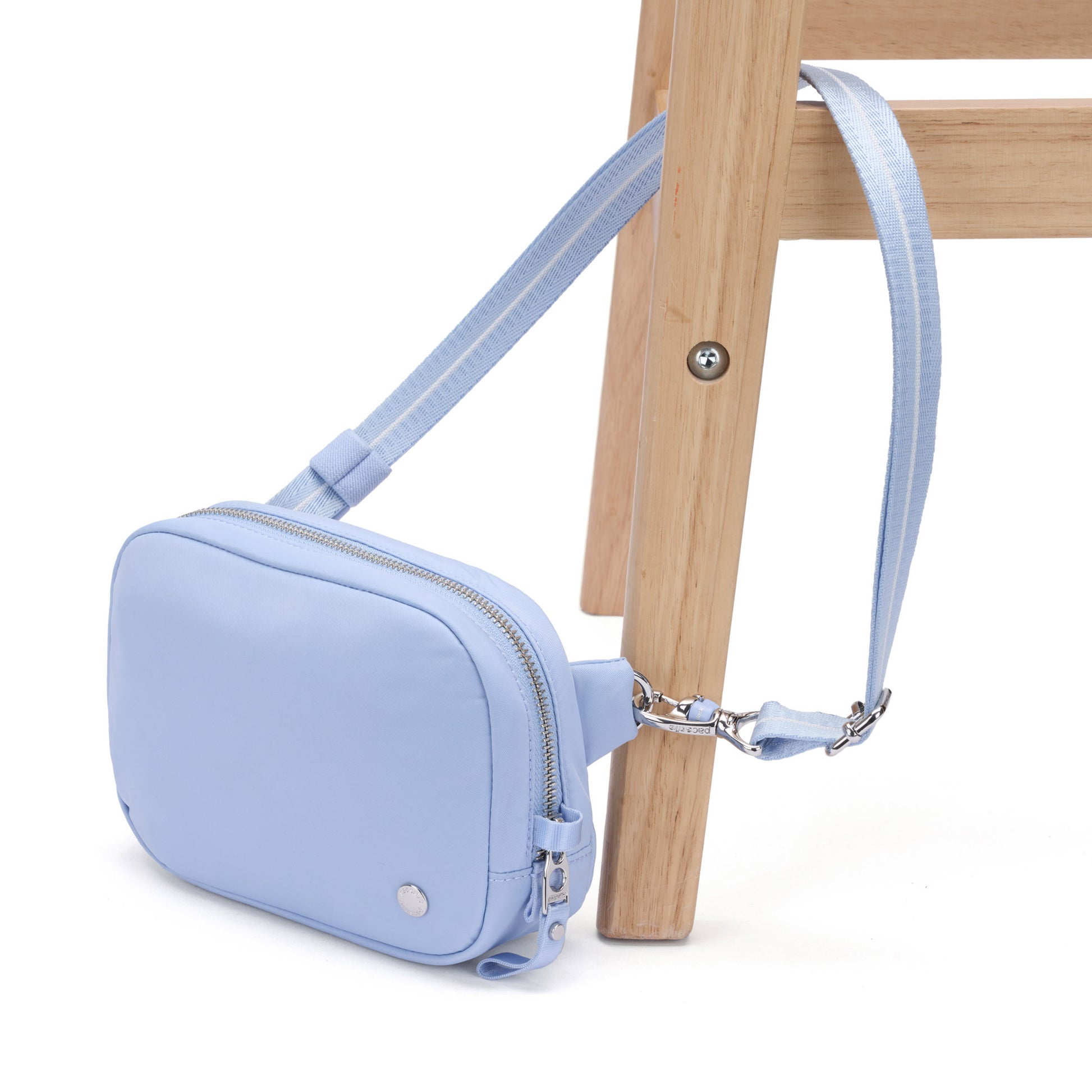 The Pacsafe® W Anti-theft Micro Sling in light blue hangs by its strap from a wooden chair leg.