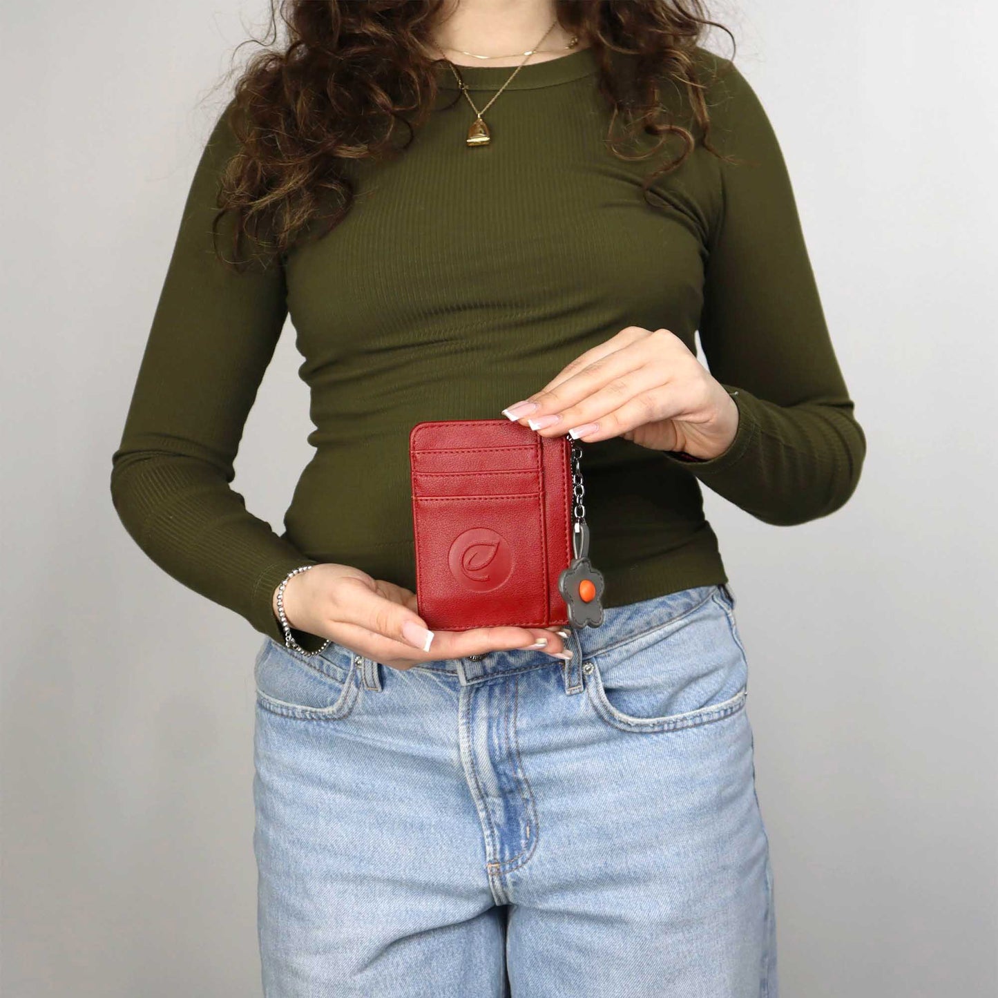 Woman wearing jeans and green long sleeve shirt holding the red Espe Pastel Card Holder in front of her