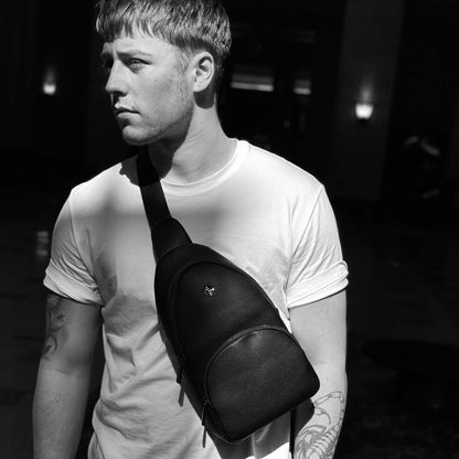 Black and white lifestyle image of man wearing white t-shirt and the Espe Raine Sling Bag in black across his chest