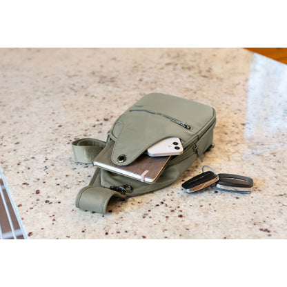 Lifestyle image of the Roots Travel Sling Bag in sage colour, laying on a marble countertop with a notebook and phone sticking out and car keys beside it.