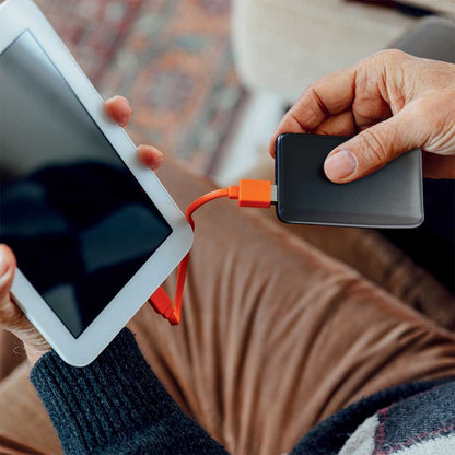 Person connecting a High Road Power Bank to a tablet with an orange USB cable for portable charging.