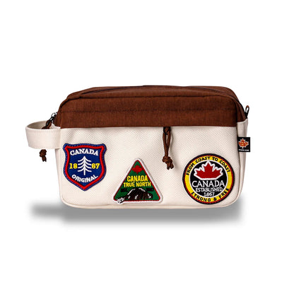 The Northern Icons Canada Travel Toiletry Bag is beige/brown with a handle and three embroidered patches.