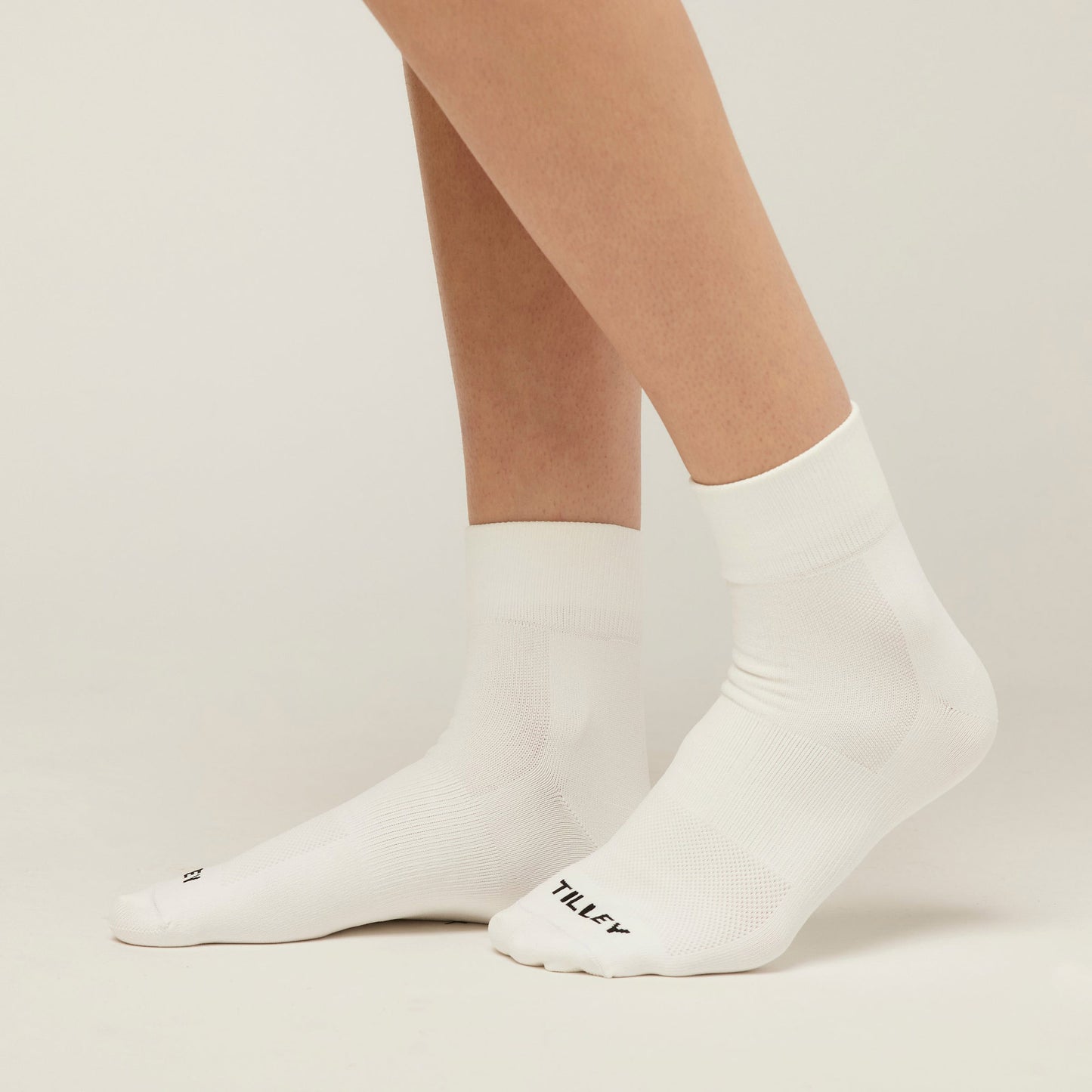 A person in white Tilley Ankle Travel Socks with arch support and toe text stands on a light surface.