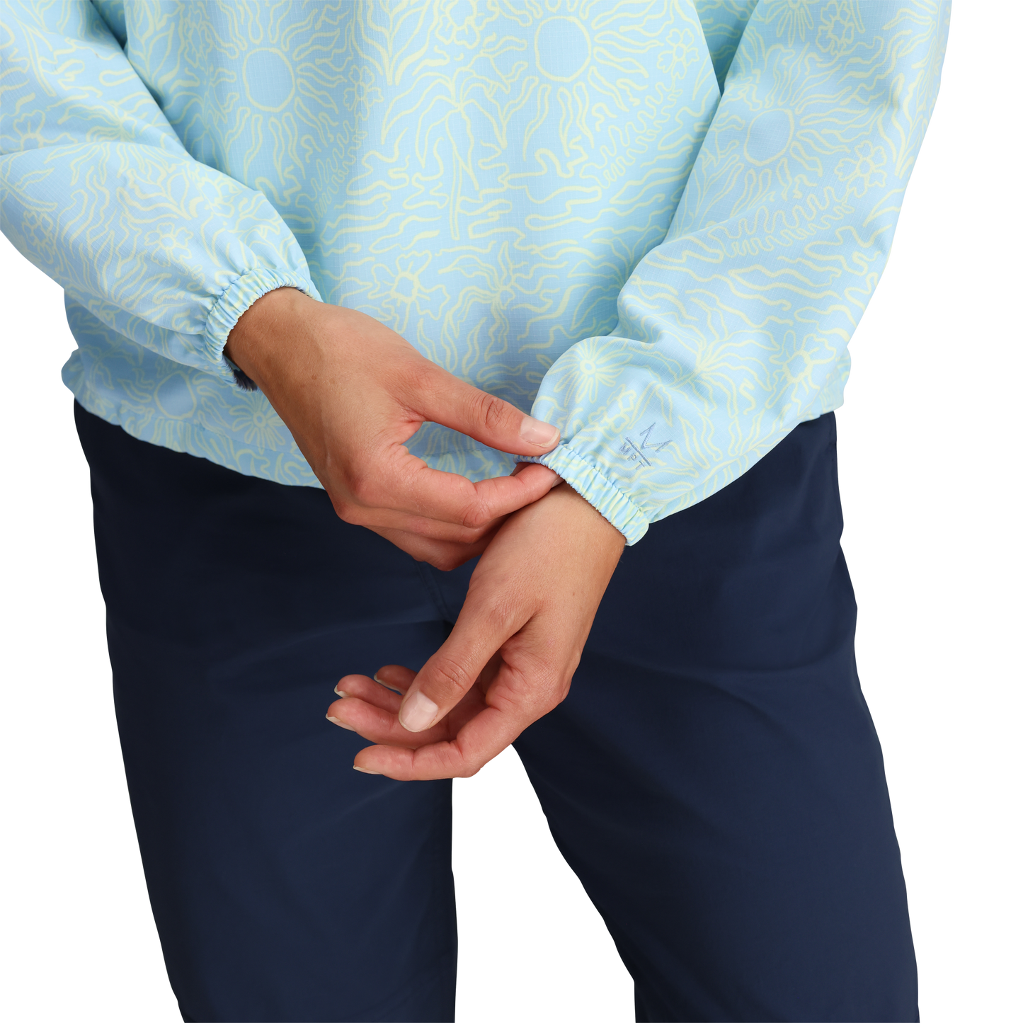 Woman adjusts the cuff of a Royal Robbins Women's Salathe Sun Hoodie, wearing dark blue pants against a plain backdrop.