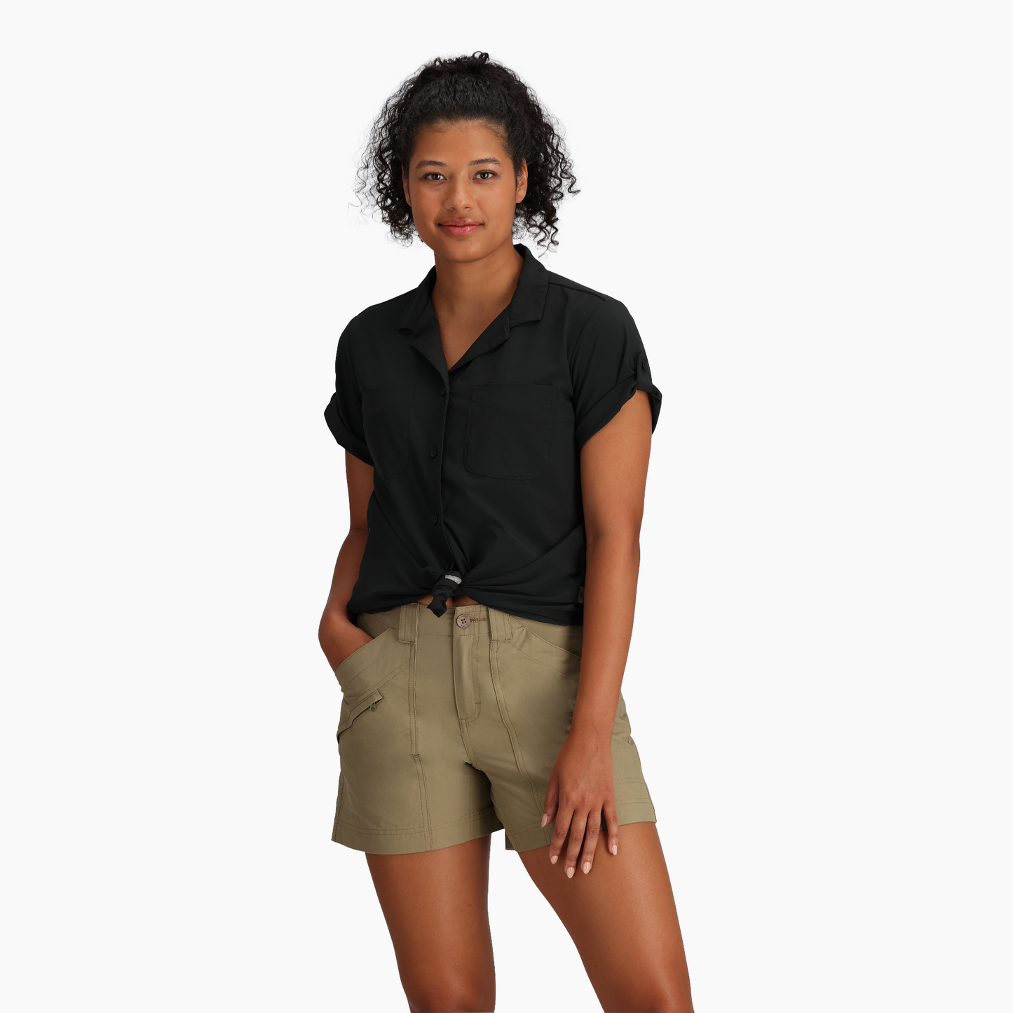 Woman wears Royal Robbins Spotless Evolution Meadow SS shirt in black and tan shorts, standing against white background.