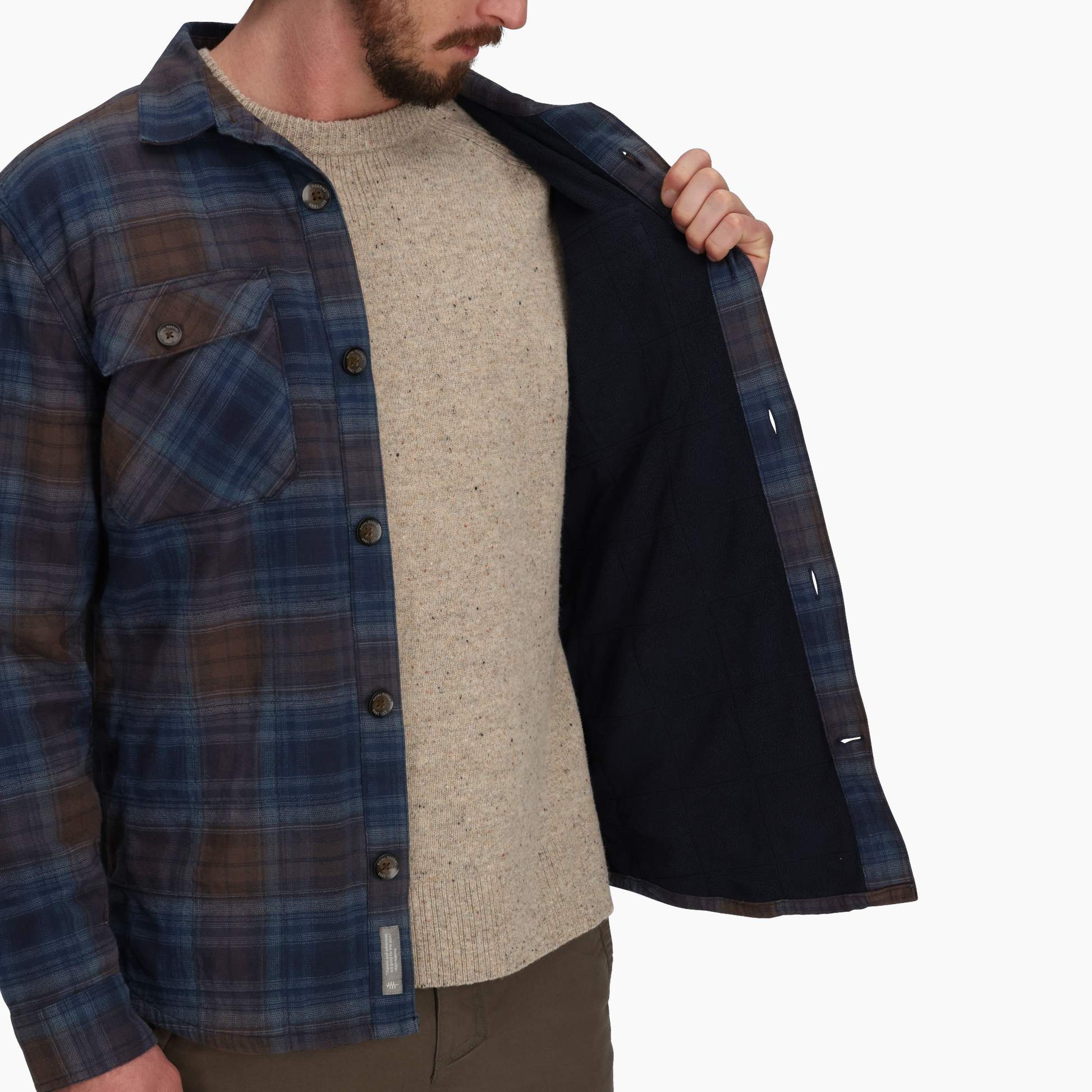 A man opens a Royal Robbins Snowcap Lined Flannel to reveal its black fleece lining, over a beige sweater.