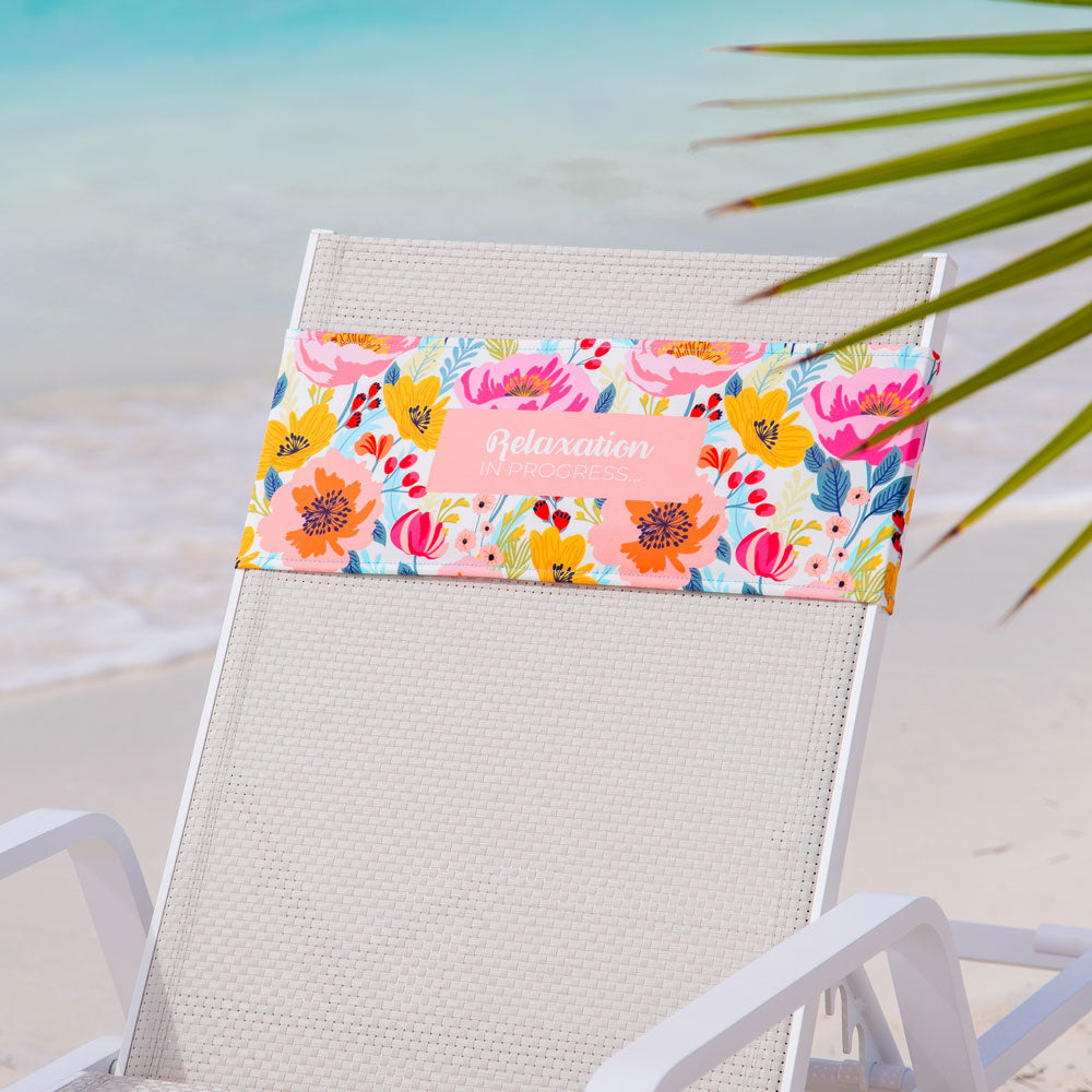 K5 Reserved Chair Sleeve on white beach chair with floral towel, "Relaxation in Progress," by the ocean.