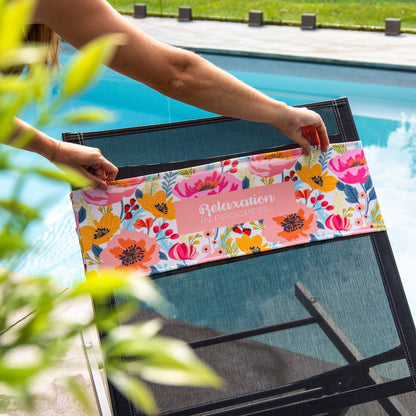 Person placing a K5 Reserved Chair Sleeve on a poolside lounge chair with a beach chair accessory.