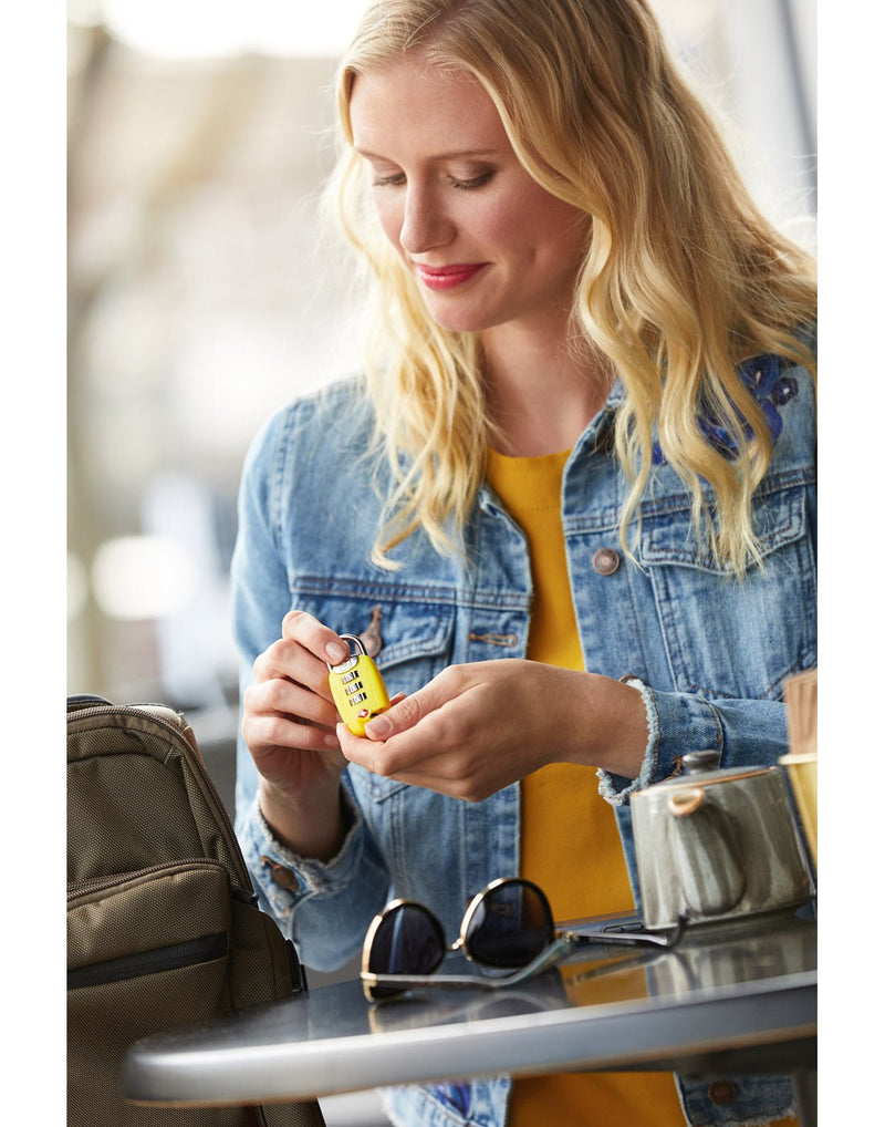 Lifestyle image of woman sitting at a table holding the Go Travel Big Dial Twist 'N' Set Combination Lock in yellow