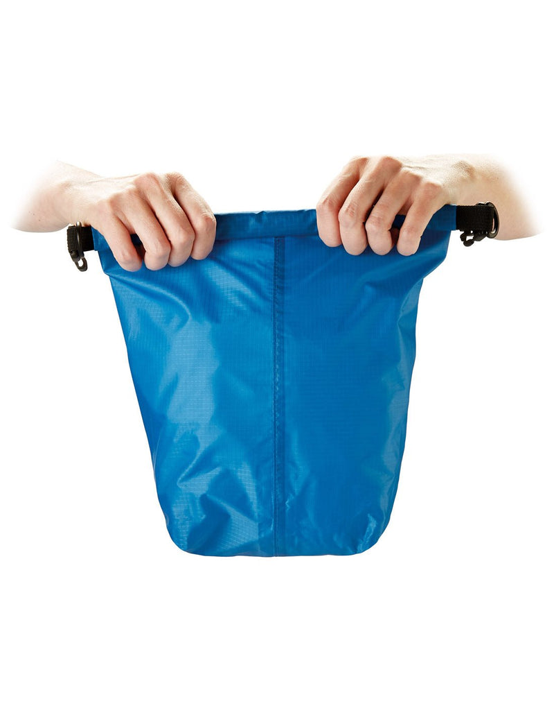 Front view of blue Go Travel Wet/Dry Bag, with hands rolling up the top to seal contents inside.