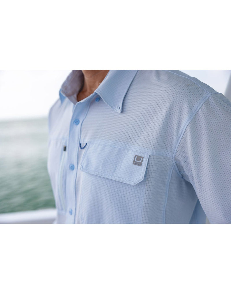 Close-up front view of a man wearing a Huk Men's A1A Button-Down Shirt in Ice Water blue colour.