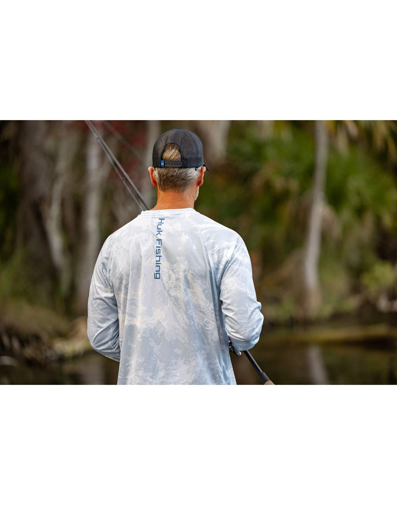 Lifestyle image upper torso  back view of a man wearing the Huk Men's Mossy Oak Pursuit Performance Shirt in Mossy Oak Stormwater Bonefish colour.