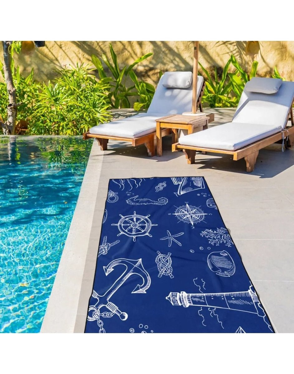 Lifestyle image of nautical K5 Microfibre Beach Towel, laid flat on the ground beside a pool with pool chairs visible in the background.