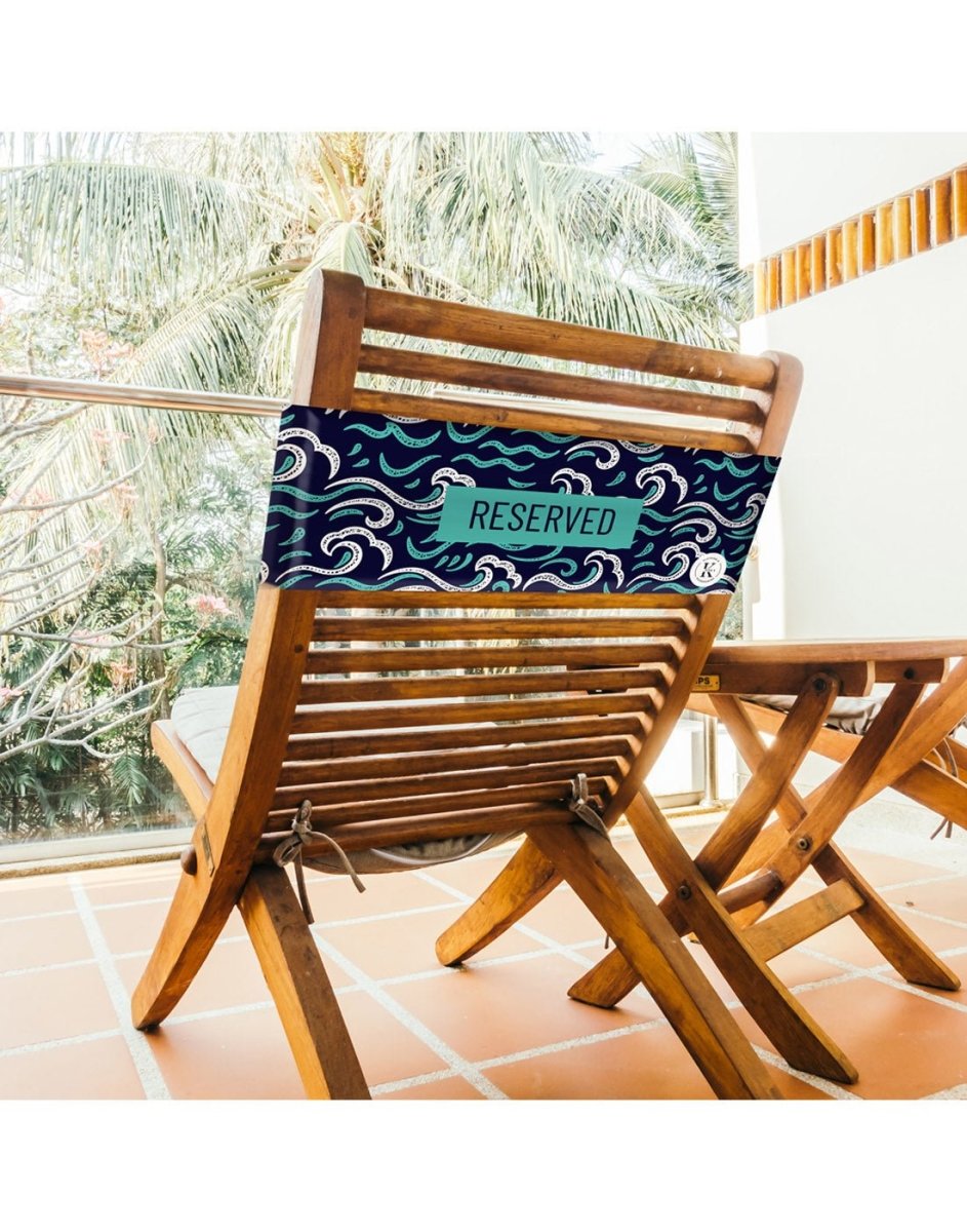 Lifestyle image of ocean K5 Reserved Chair Sleeve, placed on a outdoor wooden chair with trees visible in the background.