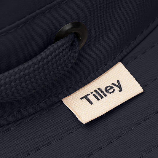 Product Image – Close-up of a dark Tilley LTM6 Airflo® Hat with mesh ventilation, beige Tilley tag, and black woven strap.