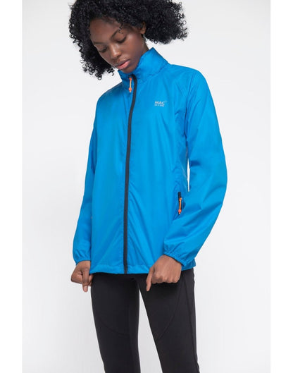 Woman wearing Mac in a Sac Origin II Packable Waterproof Jacket in ocean blue, front angle view with hands holding the bottom of the jacket.