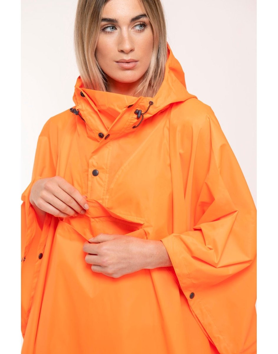 Front view of woman wearing Mac in a Sac Packable Waterproof Poncho in neon orange, opened pocket showing interior storage space.