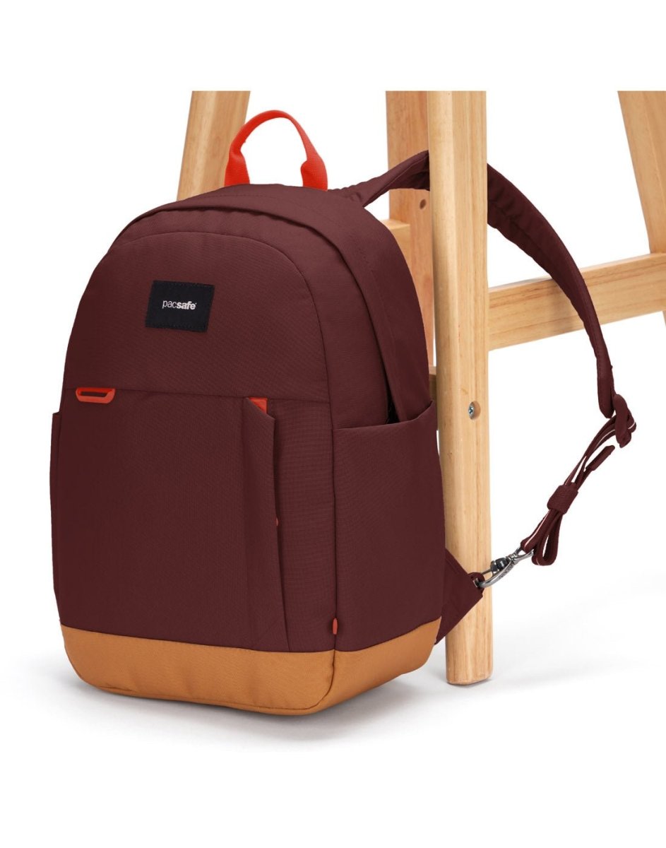 Pacsafe® Go 15L Anti-theft Backpack, garnet red with tan bottom gusset, with one strap secured to chair leg