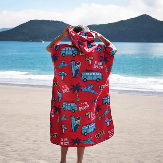 Product Image – Child on sandy beach facing ocean in a red K5 Microfibre Poncho - Kid with beach-themed prints.