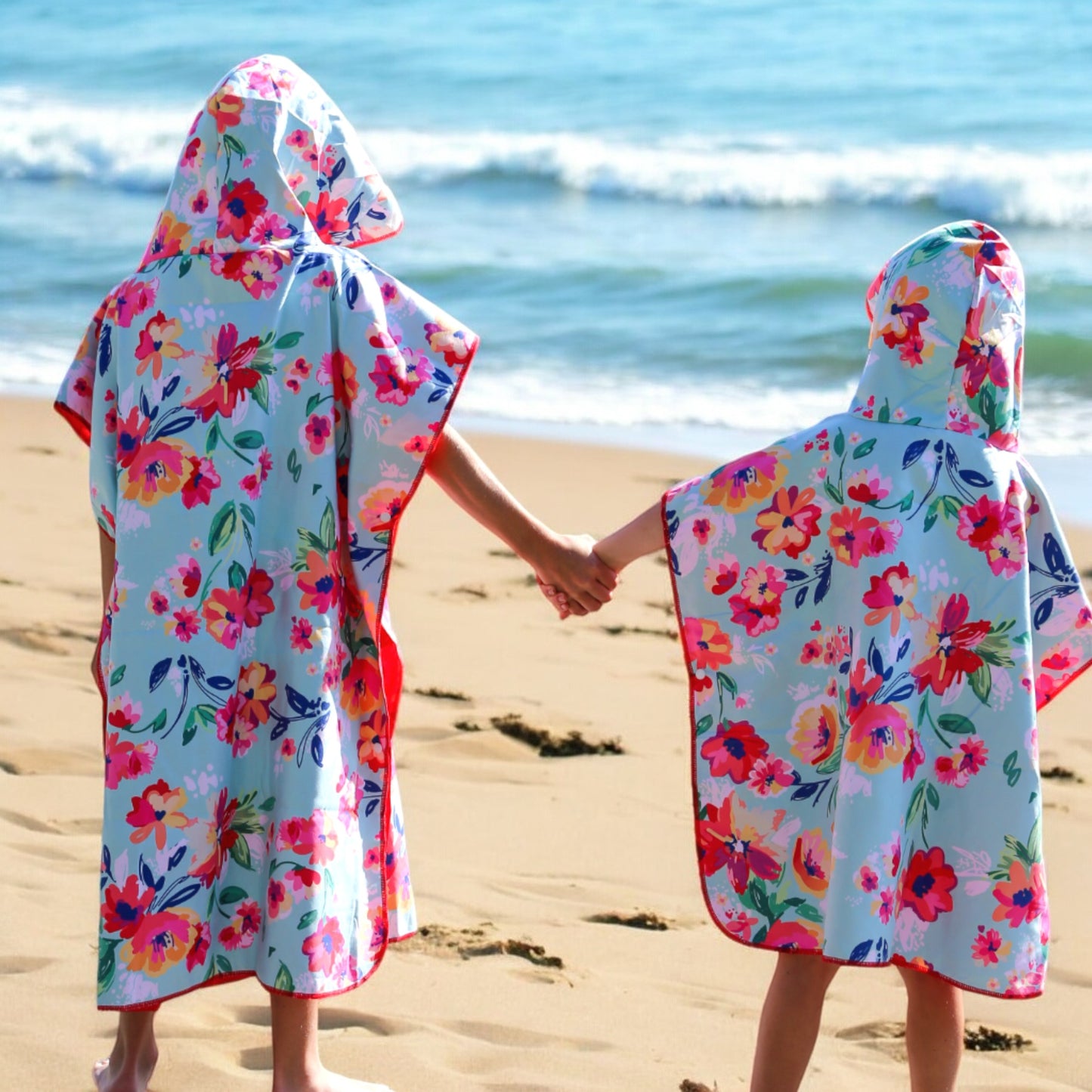 Two kids in K5 Microfibre Ponchos hold hands on the shore, gazing at ocean waves.