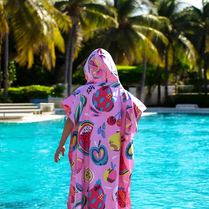 Teen wearing a K5 Microfibre Poncho stands poolside with palm trees in the background.