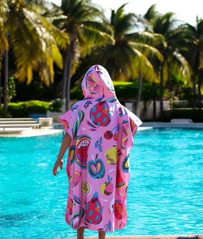 Teen wearing a K5 Microfibre Poncho stands poolside with palm trees in the background.