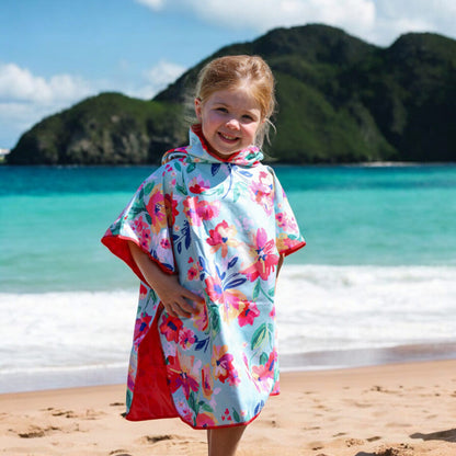 Smiling young girl wears K5 Microfibre Poncho - Kid on a sandy beach with mountains and ocean in the background.