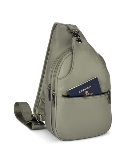 Front angle view of Roots Travel Sling Bag in sage, with front pocket unzipped and a passport placed inside.