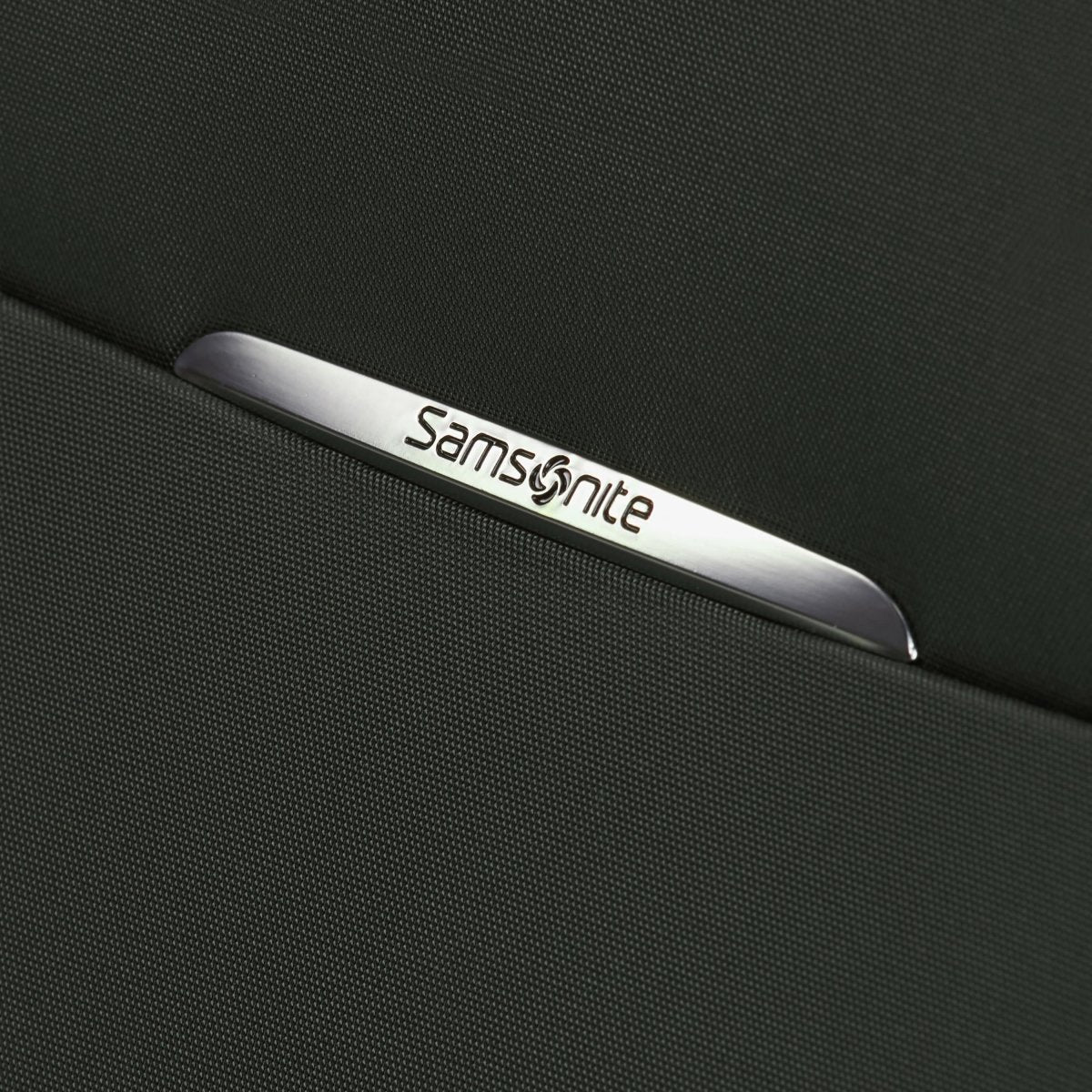 Close-up of a metal Samsonite logo on dark fabric, from the Samsonite Re-Lite Spinner Medium luggage.