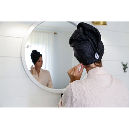 Wearing the K5 Microfibre Hair Towel, she adjusts an earring by a round mirror in soft light.
