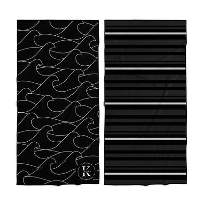 Two K5 Microfibre Beach Towels: one black with a white wave, the other black with gray stripes.