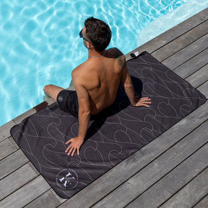 A man relaxes poolside with his feet in the water on a K5 Microfibre Beach Towel.