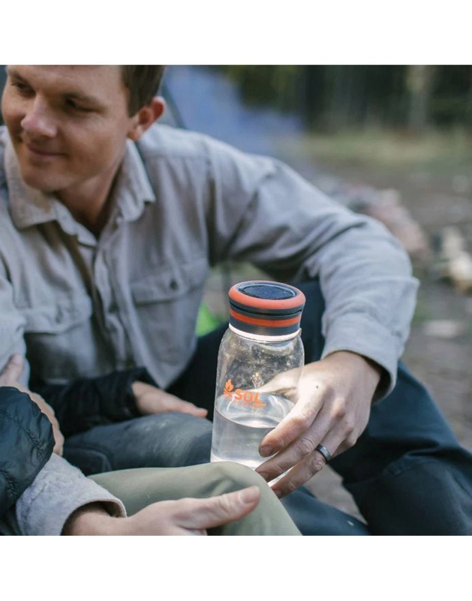 Man holding the SOL Venture Solar Water Bottle Lantern with light on and half filled with water