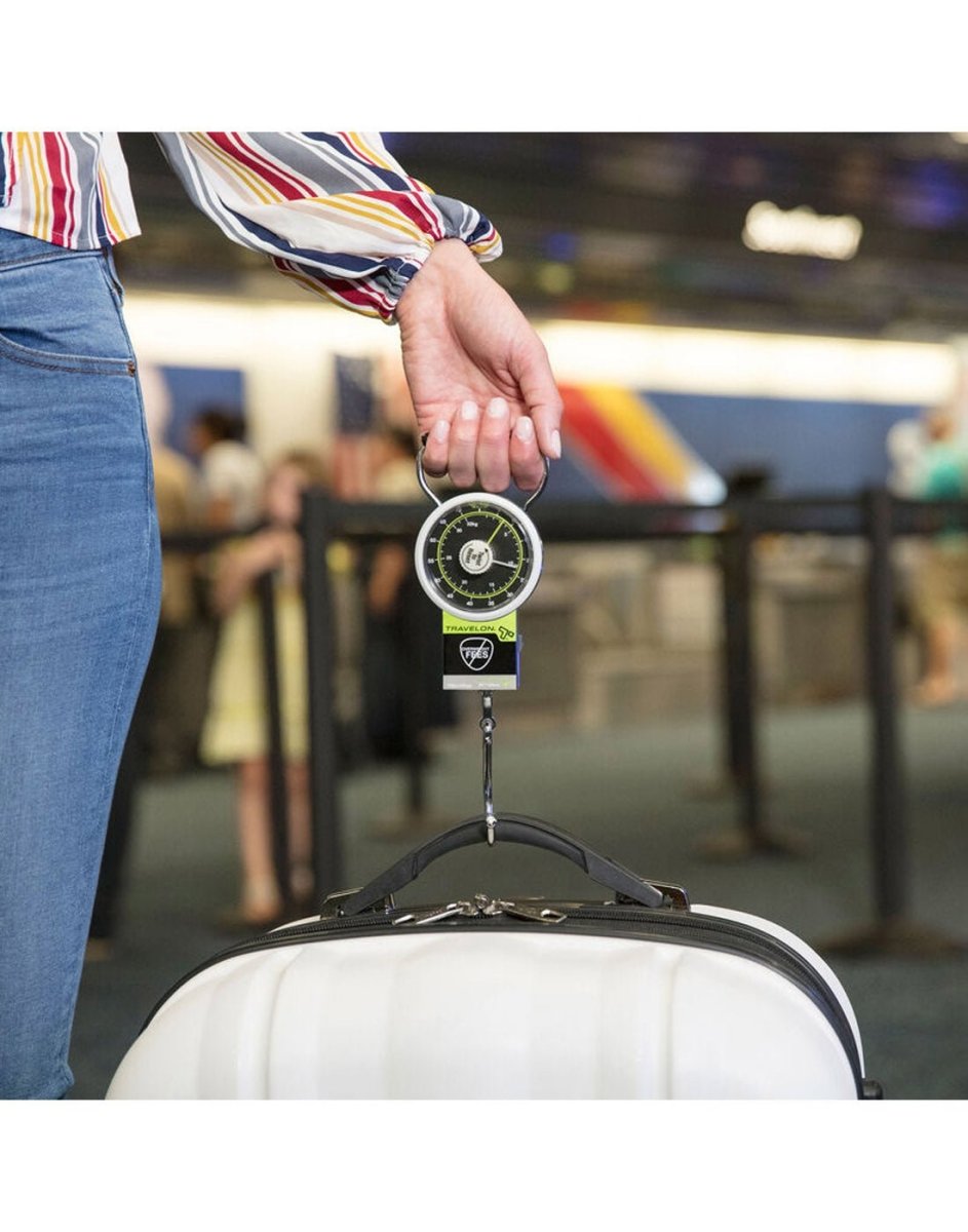 Woman holding the Travelon Stop & Lock Luggage Scale with Tape Measure in one hand with a suitcase on the hook