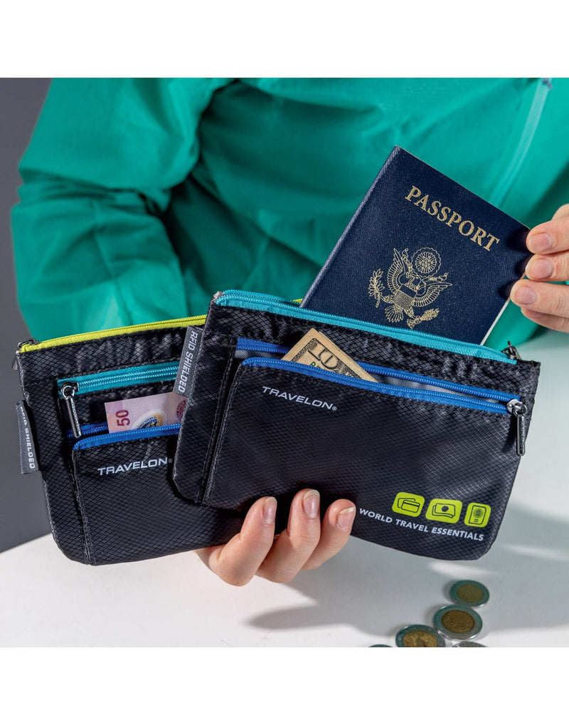 Lifestyle image of hand holding Travelon World Travel Essentials Set of 2 Currency & Passport Organizers in black, with cash and passport visible from zipper pockets.