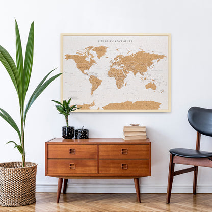 Lifestyle image of Travel Board Large World Map hanging on a wall above a side table with books and a plant on it with a large plant and chair beside