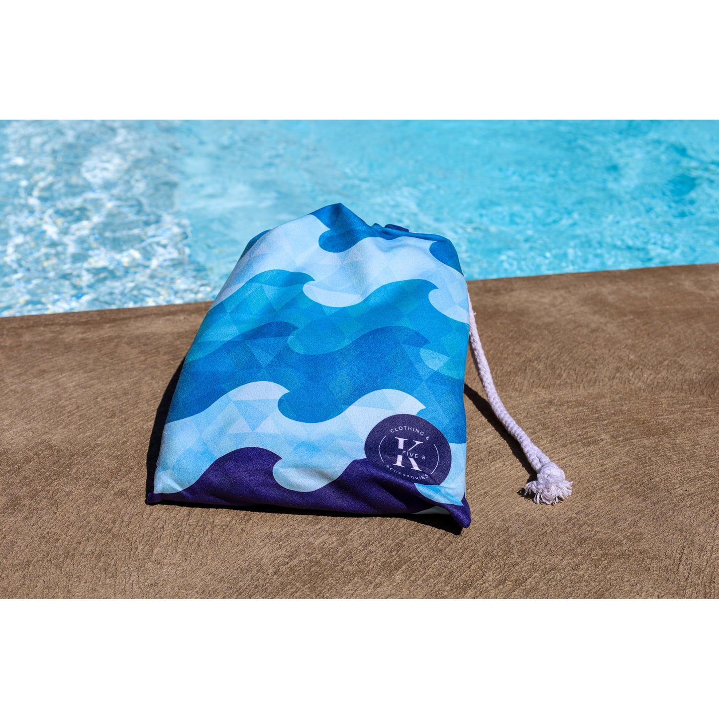 A blue patterned bag rests poolside, perfect for carrying your K5 XXL Microfibre Beach Towel by the water.