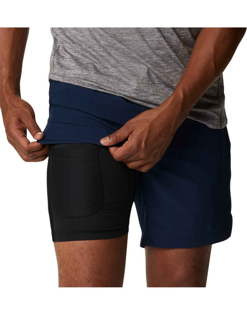 Close up of man wearing a grey t-shirt and the Columbia Men's Alpine Chill™ Zero Shorts in collegiate navy, front view, holding up the outer shell to show black inner liner shorts with thigh pocket