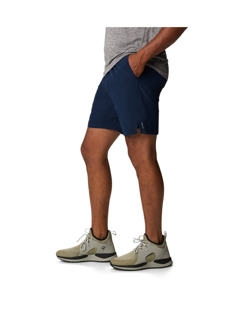 Man wearing a grey t-shirt, khaki running shoes, and the Columbia Men's Alpine Chill™ Zero Shorts in collegiate navy, side view with hands in pockets
