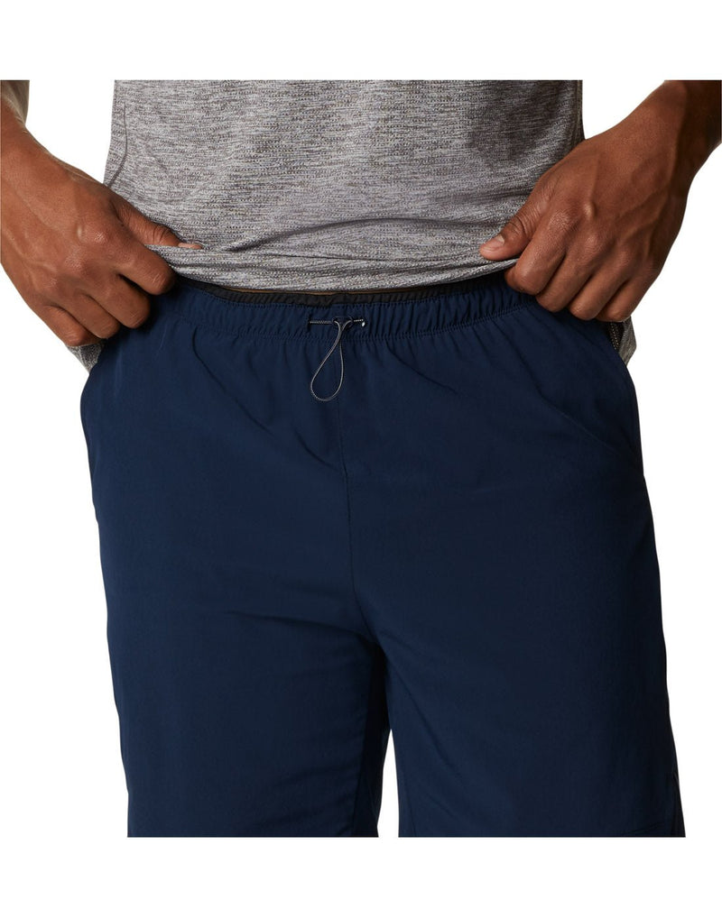 Close up of man wearing a grey t-shirt and the Columbia Men's Alpine Chill™ Zero Shorts in collegiate navy, front view, holding shirt up to show the drawstring at front centre of shorts