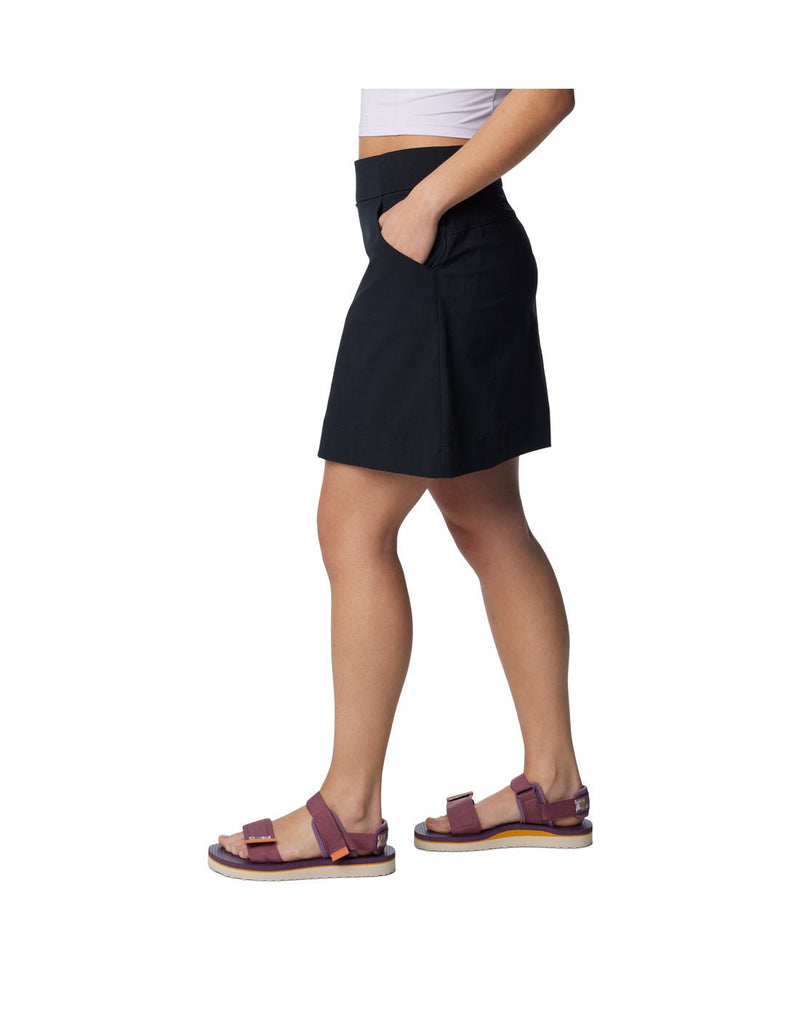 Bottom half of woman wearing purple sandals and Columbia Women's Anytime™ Straight Skort in black with one hand in pocket, side view
